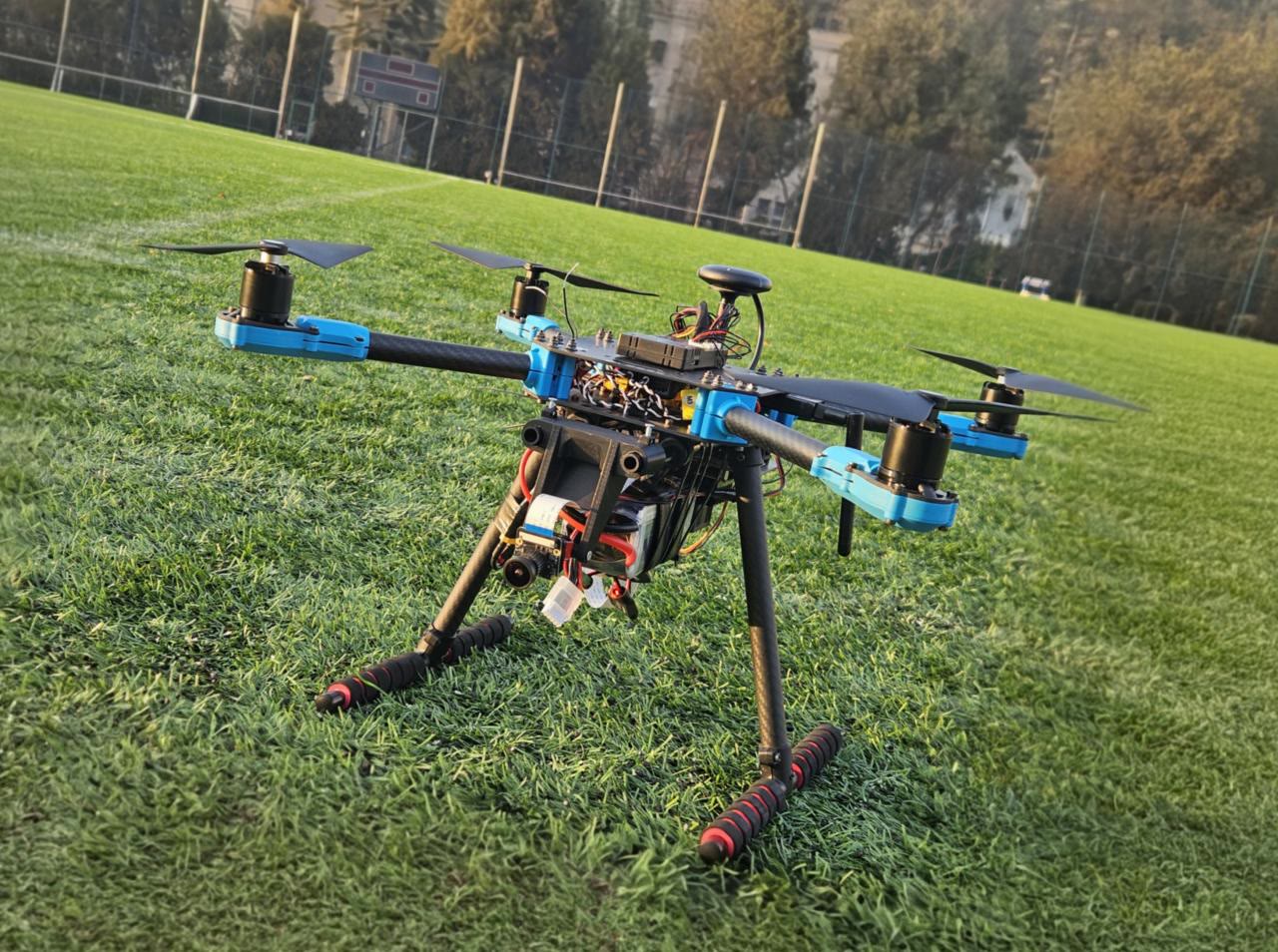 Futbol sahasının çimeninde duran, üzerinde elektronik bileşenler bulunan dört rotorlu drone.